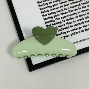Detail of light green cream-colored hair claw clip with dark green heart embellishment