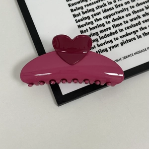 Macro detail of a high-gloss rose pink heart-shaped hair claw clip with rounded teeth