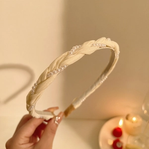 Detail of cream twisted woven headband with delicate pearl embellishments in warm lighting