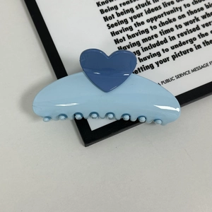 Detail view of a glossy light blue heart hair claw clip with cream finish for daily hairstyles