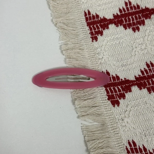 Close-up of pink oval acetate hair clip with silver metal spring buckle and French text