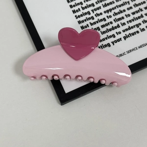 Detail of a cream pink crescent hair claw clip featuring dark pink heart accents and strong teeth