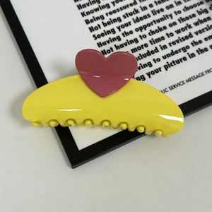 Detail shot of a glossy yellow hair claw clip with a bright pink heart accent piece