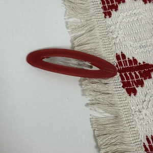 Detailed macro of a red matte oval acetate hair clip with silver metal spring component