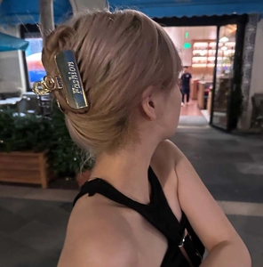 Dettaglio della molletta per capelli in metallo dorato con scritta Fashion e logo C