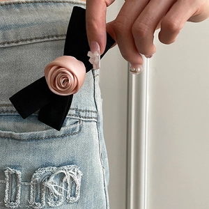 Elegant black bow hair clip with pink silk rose accessory on blue denim background