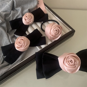 Detail view of pink satin rose hair clips with black textured ribbon bows and hair tie