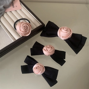 Detail of pink satin rose scrunchie and black ribbon bow hair clips set on a surface