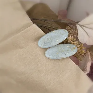 Détail de barrettes ovales en résine bleu clair avec feuilles d'or sur fond vintage