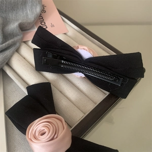 Detail of handmade black fabric bow hair clip featuring a soft pink satin rose centerpiece