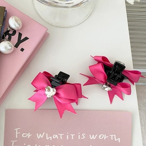 Détail de barrettes à nœud rose avec strass en forme de cœur et petite griffe en plastique