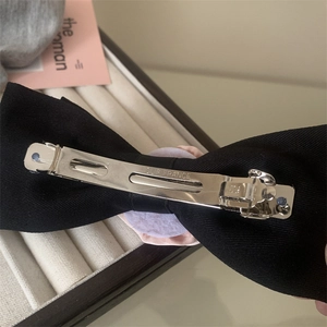 Close-up of black bow hair clip featuring a silver metal spring clip with France engraving