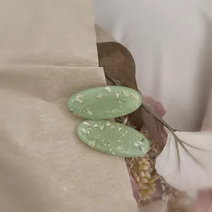 Détail de pinces à cheveux ovales en résine vert menthe avec paillettes dorées sur papier