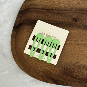 Détail de trois jolies barrettes BB vert pastel posées sur un plateau en bois brun