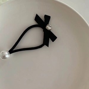 Détail d'un élastique noir avec un nœud, une perle blanche et un charme cœur en strass