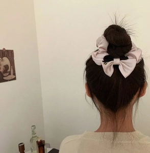 Detailansicht eines rosa Satin-Haargummis mit schwarzer Schleife an einem Dutt