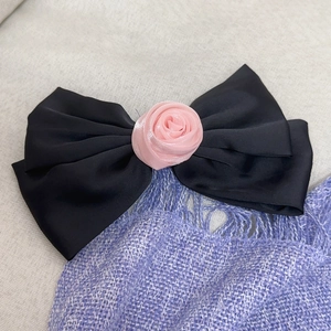 Dettaglio dell'elegante fiocco per capelli in raso nero con una delicata rosa in tessuto