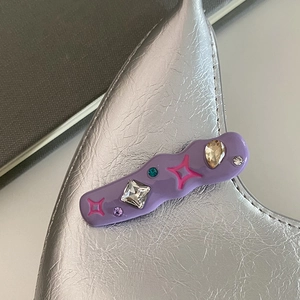 Détail d'une pince à cheveux lilas ondulée avec cristaux et motifs d'étoiles