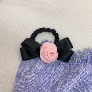 Dettaglio ravvicinato di una rosa di raso rosa e un fiocco nero su un elastico per capelli