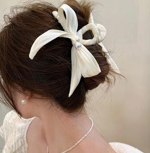 Détail d'une pince à cheveux avec nœud en soie et pendentif perle sur chignon chic