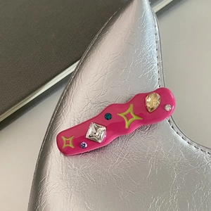 Gros plan sur une pince à cheveux rose ondulée Y2K avec strass colorés sur sac argenté