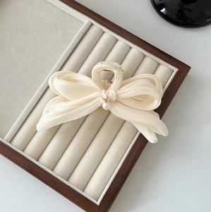Détail d'une pince à cheveux avec nœud en mousseline beige et perle dans un présentoir