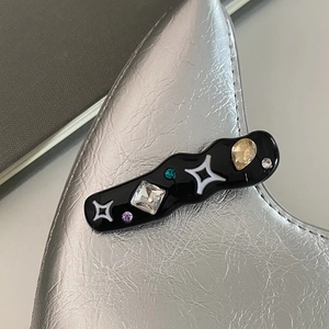 Gros plan sur la barrette noire ondulée avec strass scintillants et détails d'étoiles blanches