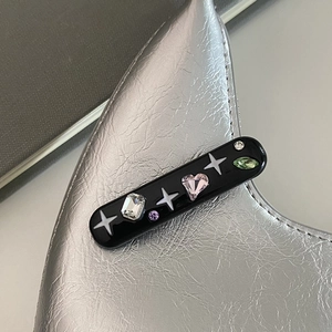 Détail macro d'une pince à cheveux noire avec strass colorés sur un sac argenté