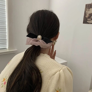 Détail d'un chouchou en organza rose avec perle et nœud noir sur une queue de cheval basse