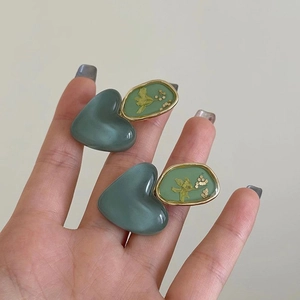 Detailed close-up of handmade green heart earrings with embedded dried yellow flowers