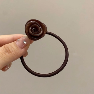 Detail of a dark brown resin rose hair tie with a glossy ceramic finish on a hand