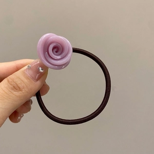 Detail of a purple resin rose hair tie held by hand against a clean light background