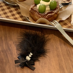 Elegant black feather hair clip with ribbon bow and heart rhinestones on a wooden surface