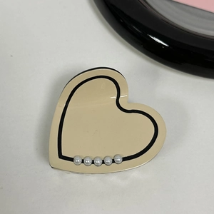 Close-up of heart-shaped hair claw clip with beige finish, black trim and pearl accents