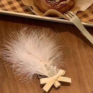 Elegant white feather bow hair clip with rhinestones displayed on a warm wooden table