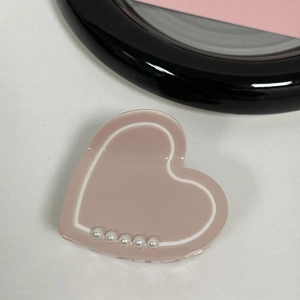 Close-up of pink heart-shaped hair claw with white pearl accents and polished finish