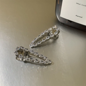 Detail of silver drop-shaped hair clips with sparkling cubic zirconia on a warm metallic surface
