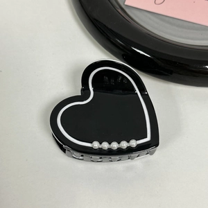 Detail view of heart-shaped black hair claw clip with pearls and white contrast edges
