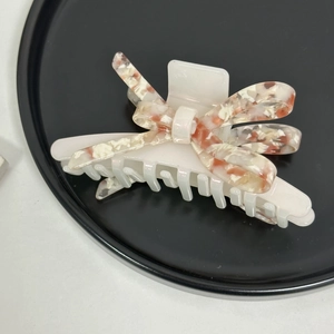 Détail d'une grande pince à cheveux nœud en acétate avec motif ambre sur un plateau