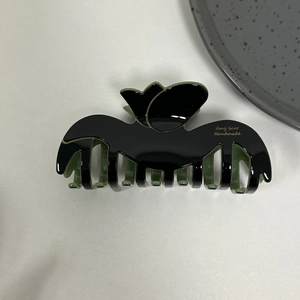Detail of tulip-shaped acetate hair claw clip in black and dark green colorway