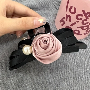 Détail d'une pince à cheveux rose satinée avec nœud noir et accents de perles