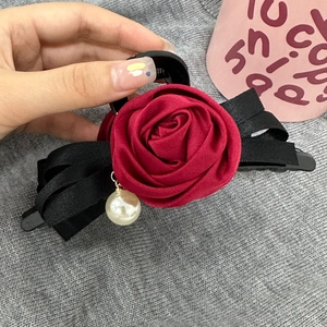 Détail de la pince à cheveux rose rouge avec nœud en ruban noir et perle blanche