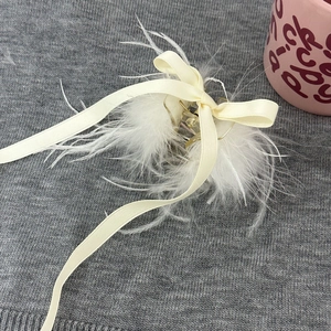Détail de la pince à cheveux en plumes blanches avec nœud en ruban crème élégant