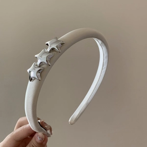 Dettaglio del cerchietto imbottito beige con tre stelle in metallo argentato