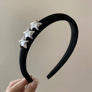 Dettaglio del cerchietto in velluto nero con tre ciondoli a stella argentati e texture morbida