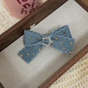 Vintage Y2K denim bow hair clip with gold stars and rhinestone center on wooden tray