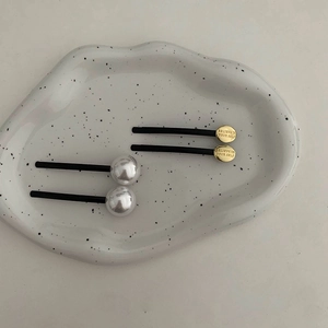 Dettaglio di fermagli per capelli neri minimalisti con perle e dischi dorati incisi sul vassoio