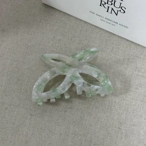 Dettaglio della molletta a farfalla in acetato marmorizzato verde su tessuto beige