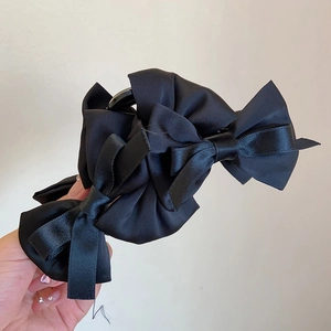Detail of a large black satin bow hair claw clip showing layered fabric texture and shine