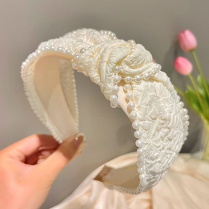 Detail of cream white headband featuring embossed fabric texture and pearl decorations